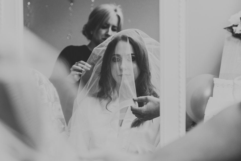 bride having her veil put on in the mirror before her wedding