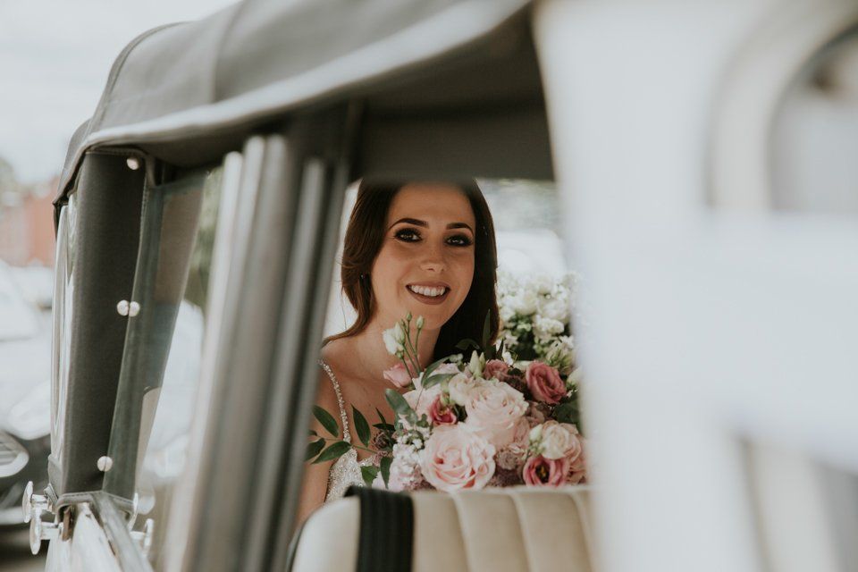bride holding flowers in the back seat of a wedding car