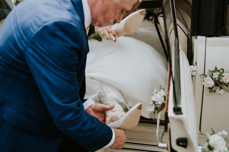 brides father helping to put his daughters shoes on in a wedding car