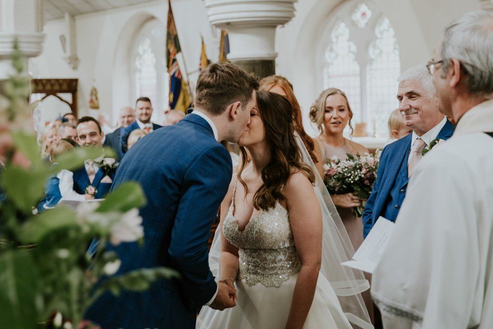 bride and groom having first kiss and holding hands at church wedding ceremony