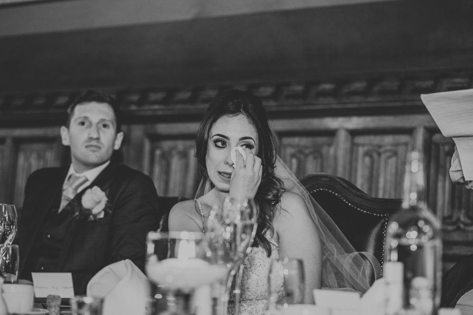 bride sat next to groom on top table wiping a tear from her eye