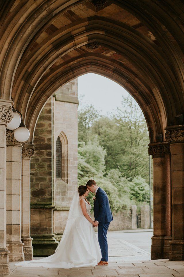 bride and groom standing touching heads and holding hands under an arch way