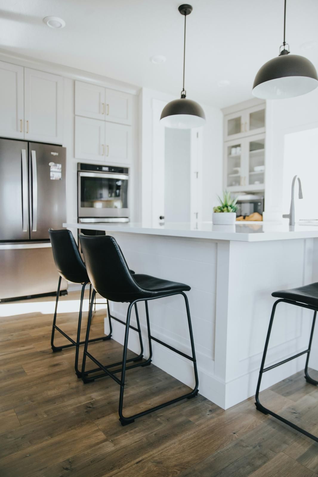 Modern kitchen with white cabinets, island with black stools, stainless steel appliances, and wood floor.