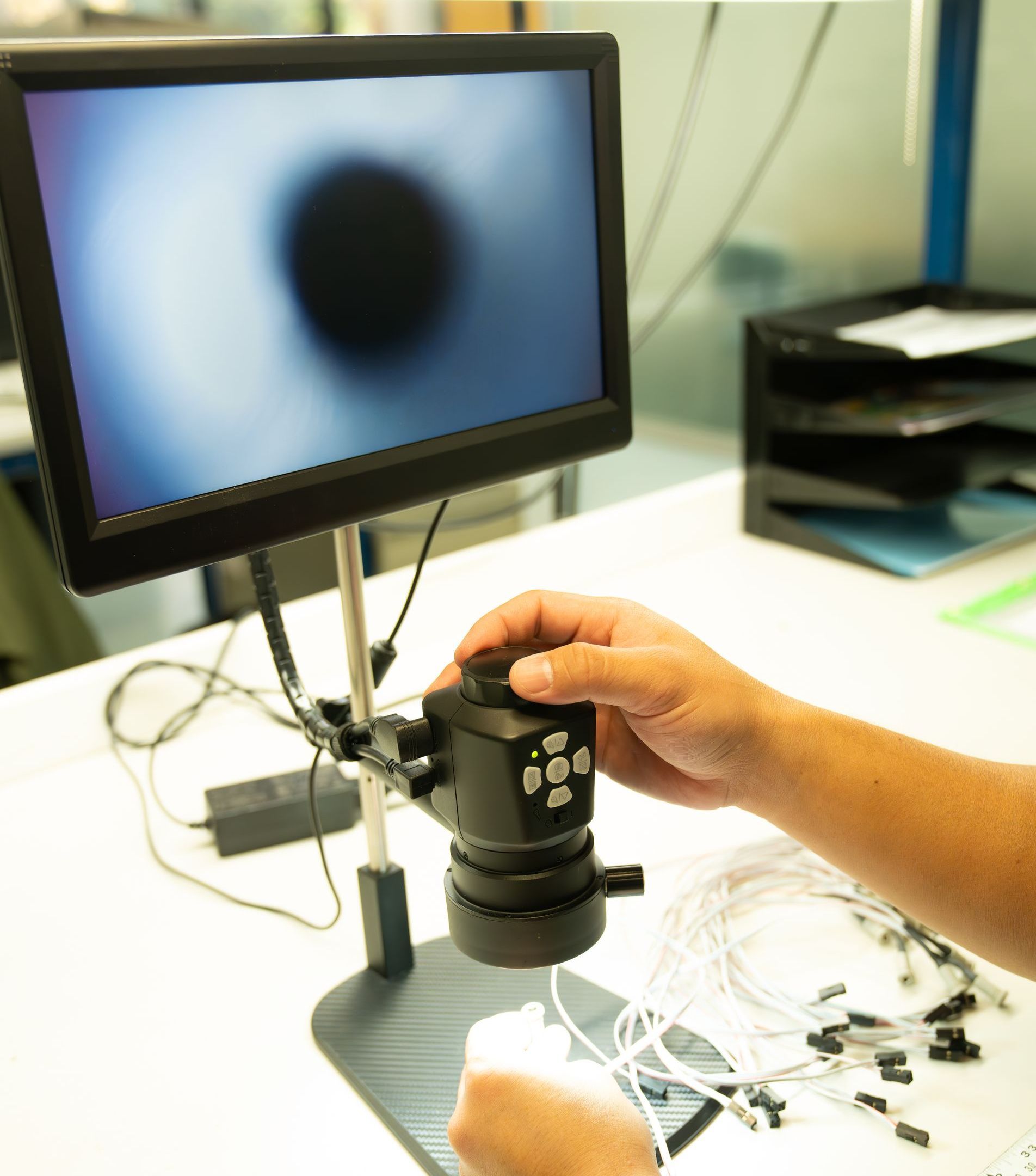 A person is using a microscope in front of a computer monitor