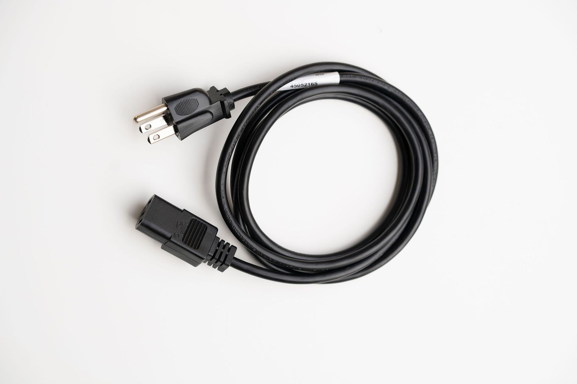 A black power cord is sitting on a white surface.