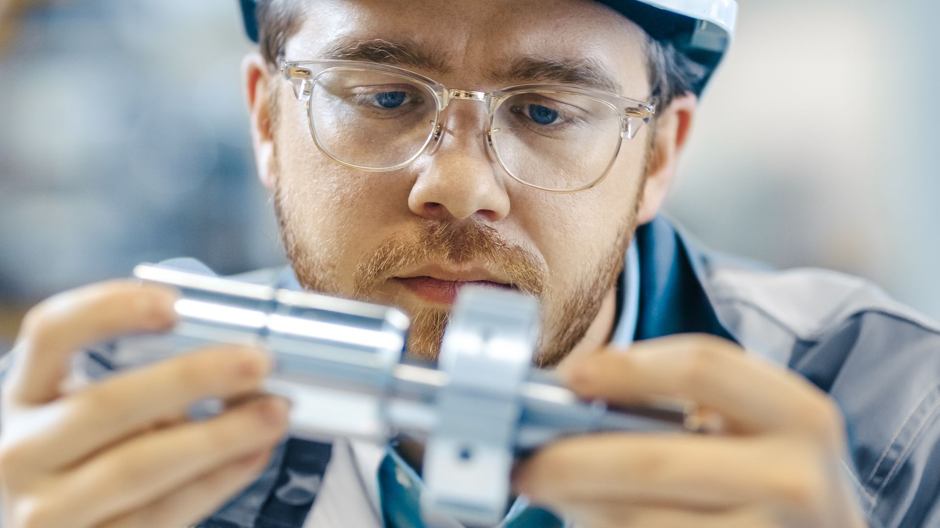 A man wearing glasses and a hard hat is holding a metal object in his hands.
