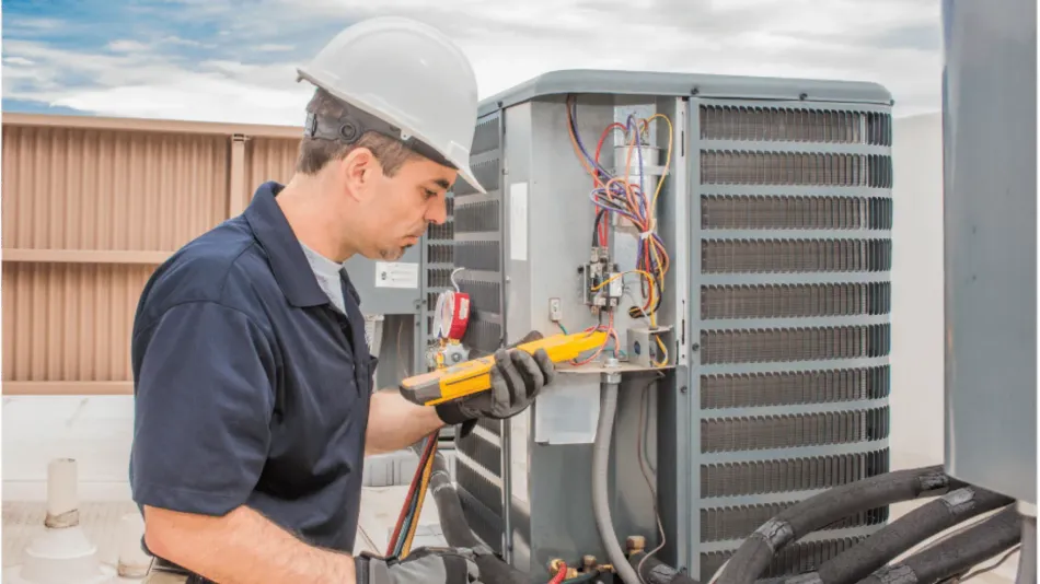 HVAC technician in hard hat inspects an air conditioning unit with a yellow multimeter outdoors.