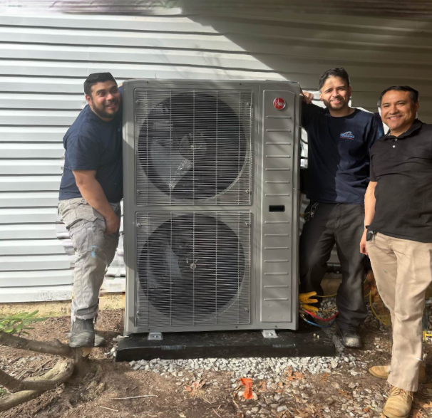 Three men pose beside a large air conditioning unit mounted on a gravel base.