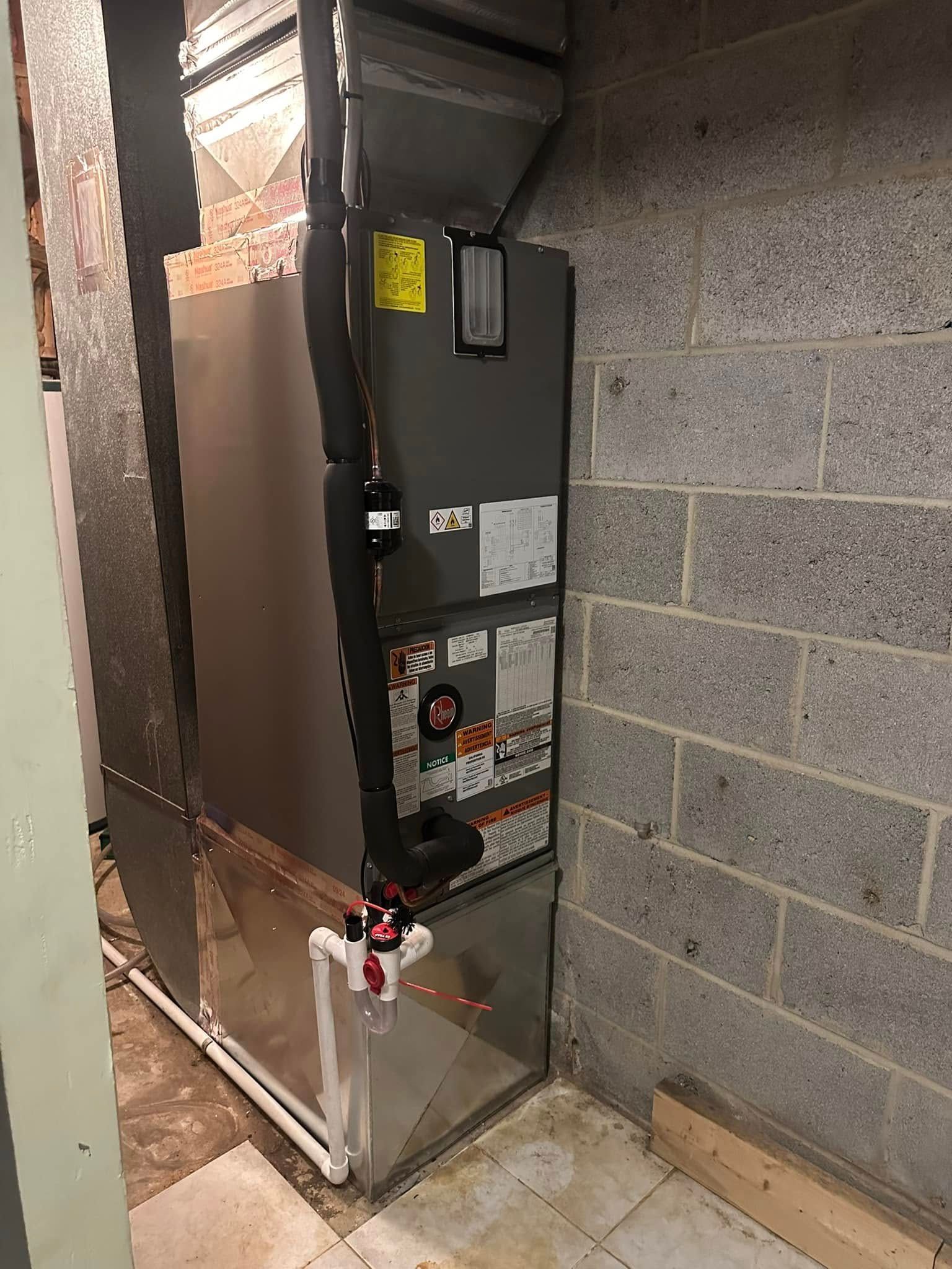 Furnace unit in a basement, gray metal with black pipes and white PVC.