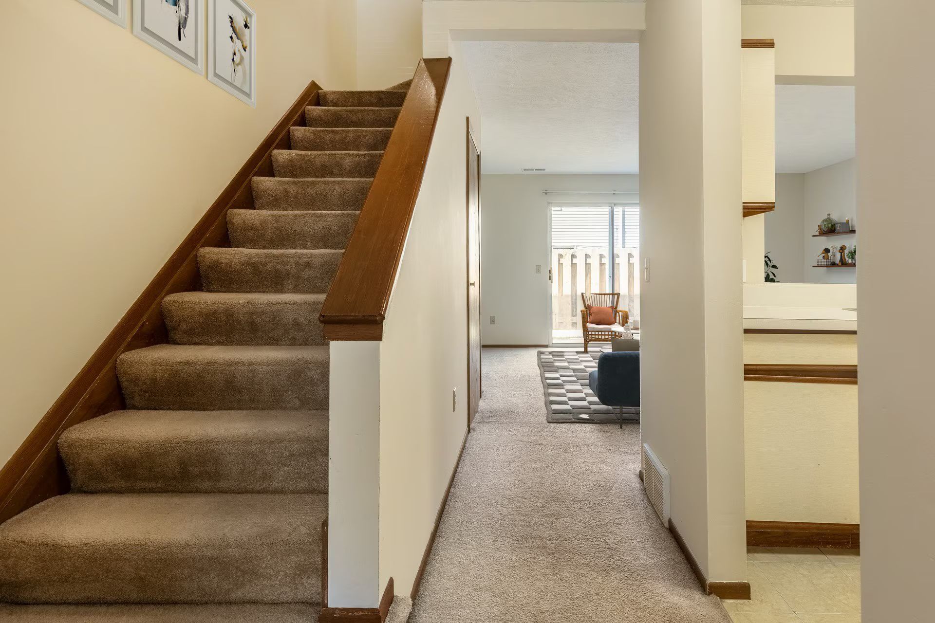 Staircase with carpet leads up. Hallway view with a living room, neutral colors.