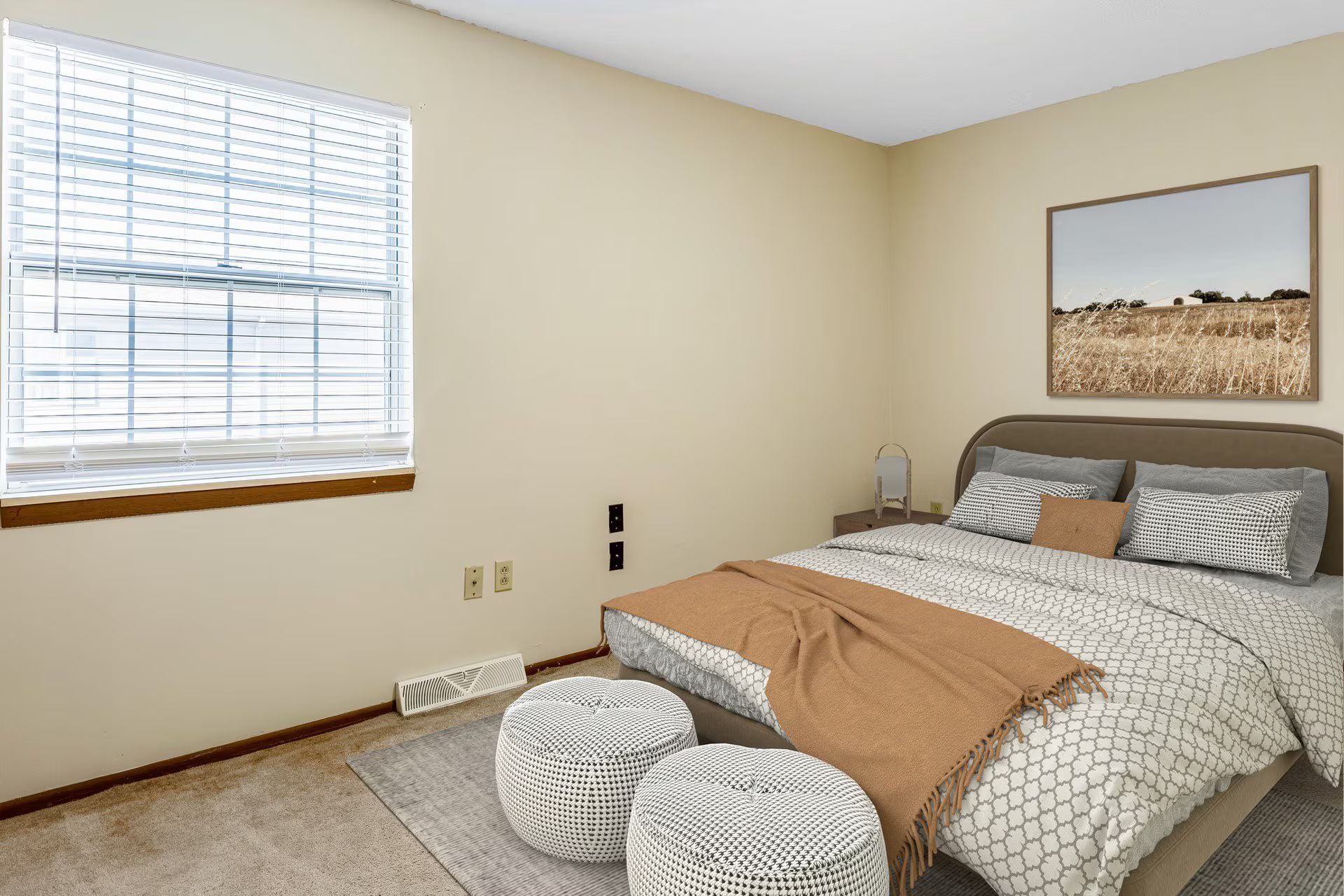 Bedroom with bed, window, neutral colors, and artwork. Two round poufs in front of the bed.