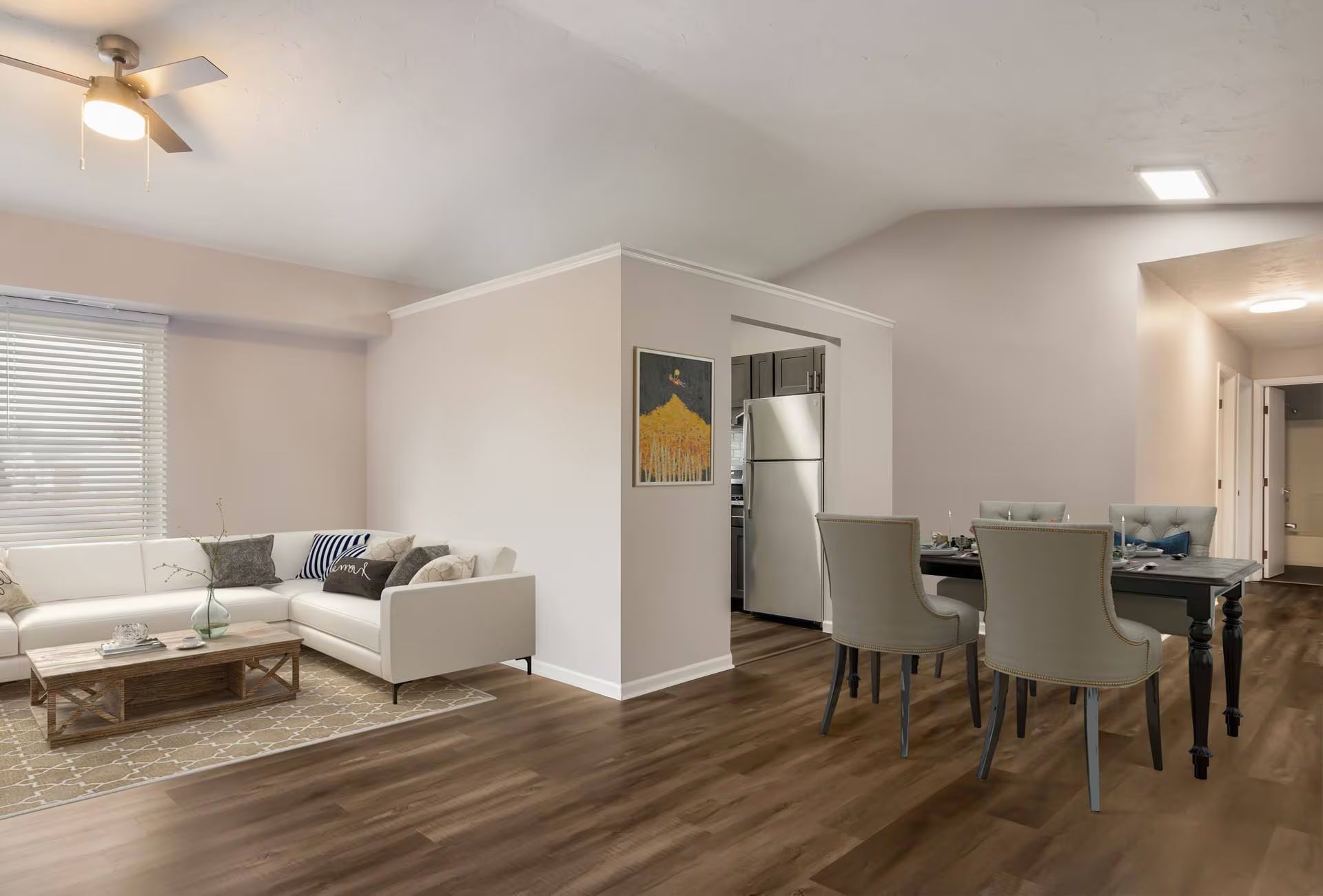 Open-concept living space with white sectional sofa, dining table, and kitchen access.