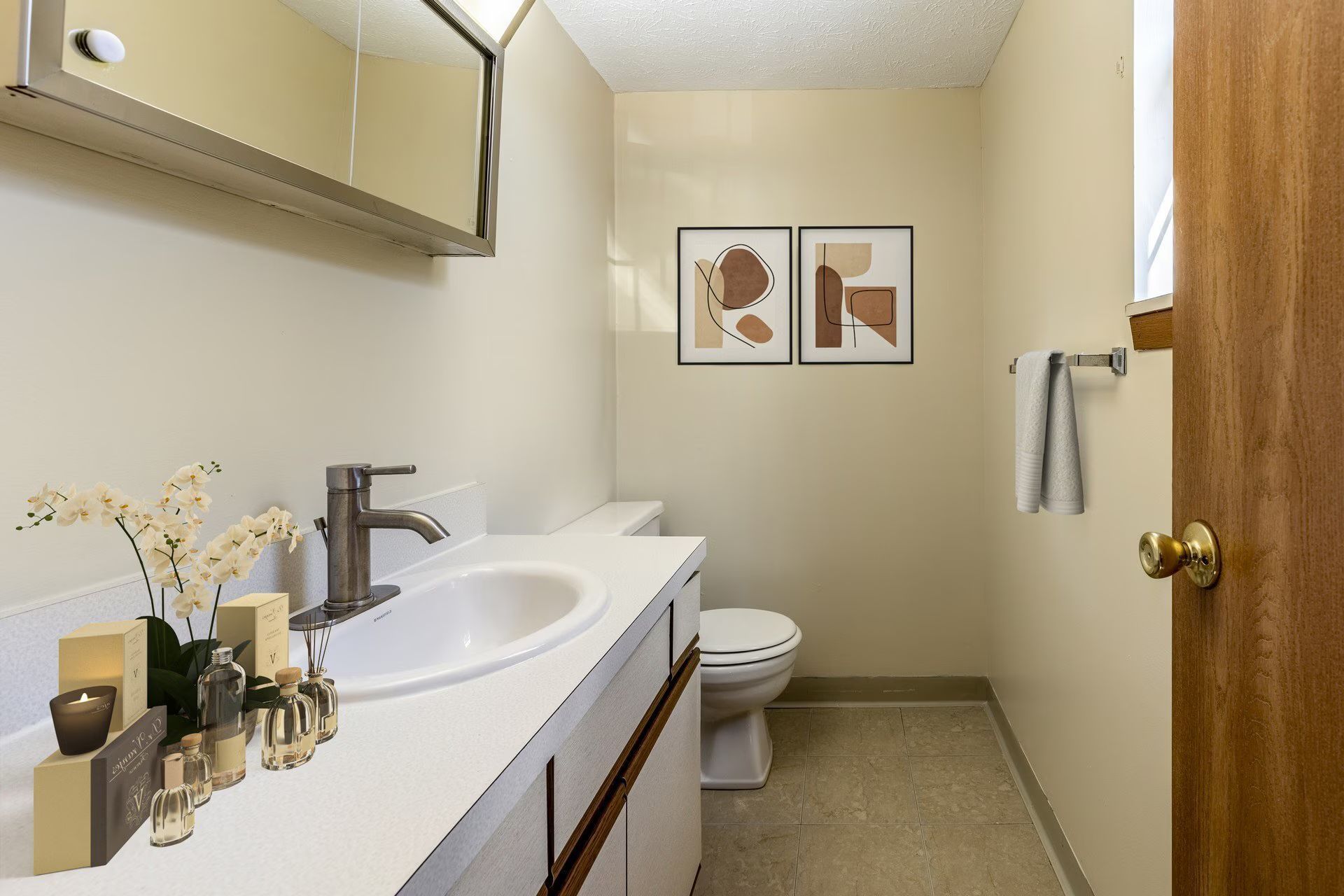 Bathroom with white vanity, toilet, and artwork. A towel hangs on a chrome bar. Door on the right.