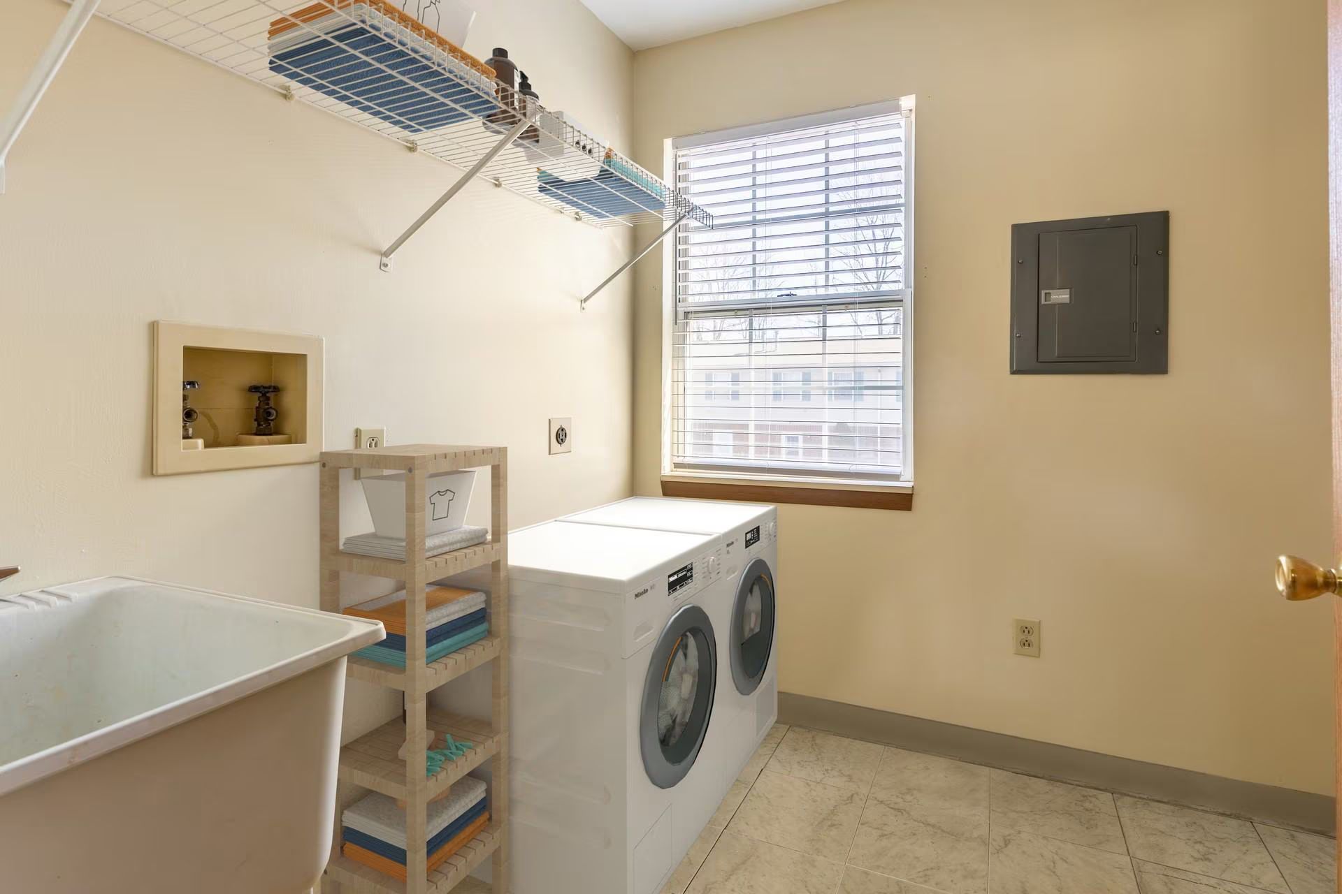Laundry room with washer and dryer, laundry sink, shelves, window, and wall-mounted drying rack.