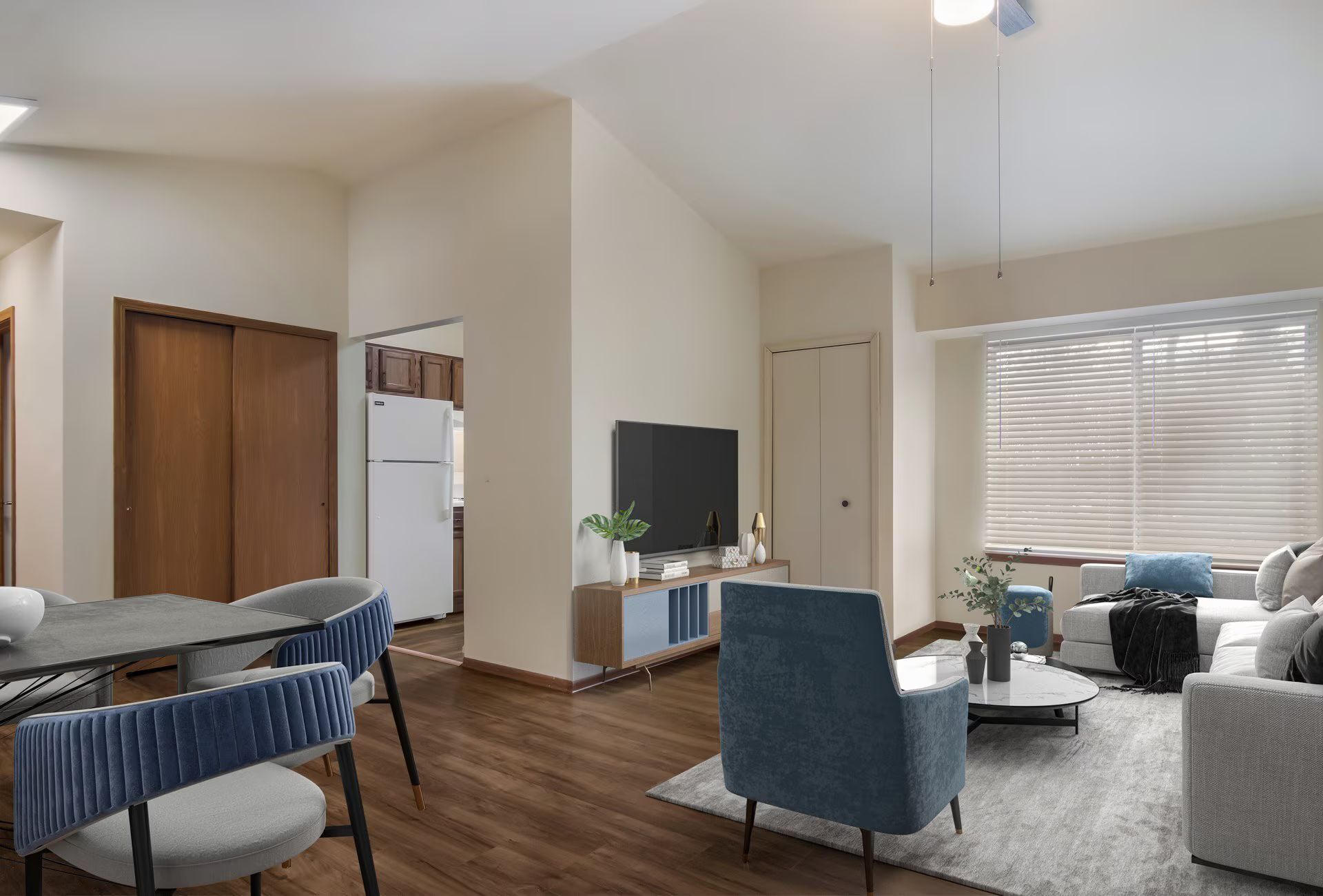 Living room with dining area. Dark wood floors, blue chairs, white walls, TV, and large window.