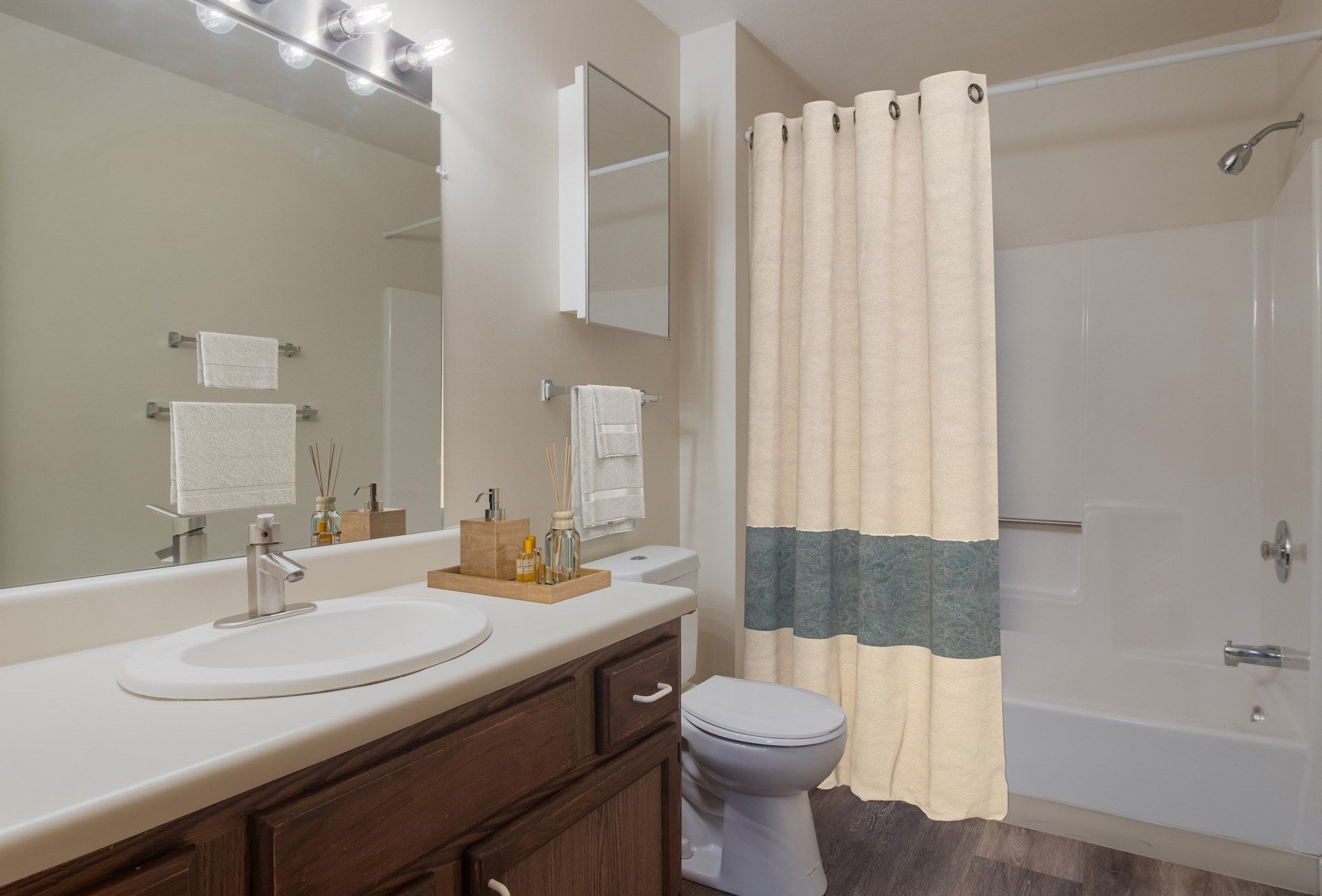 Bathroom with a sink, mirror, toilet, and shower with a beige and teal curtain.