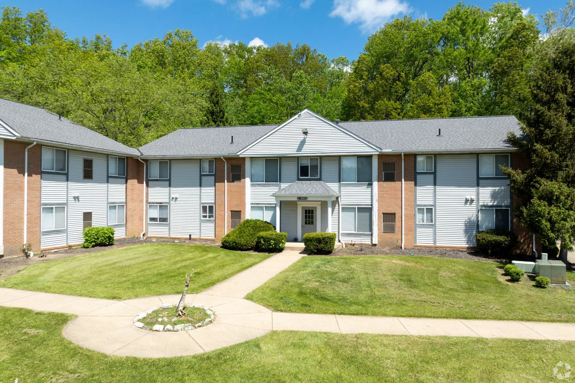 Apartment building with light blue siding, red brick accents, and green lawn.