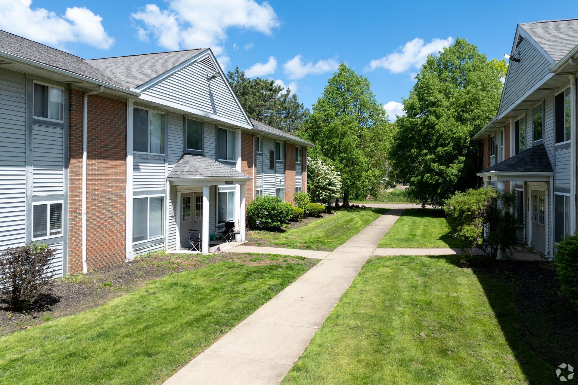Apartment buildings with gray siding, brick, and walkways on a sunny day.