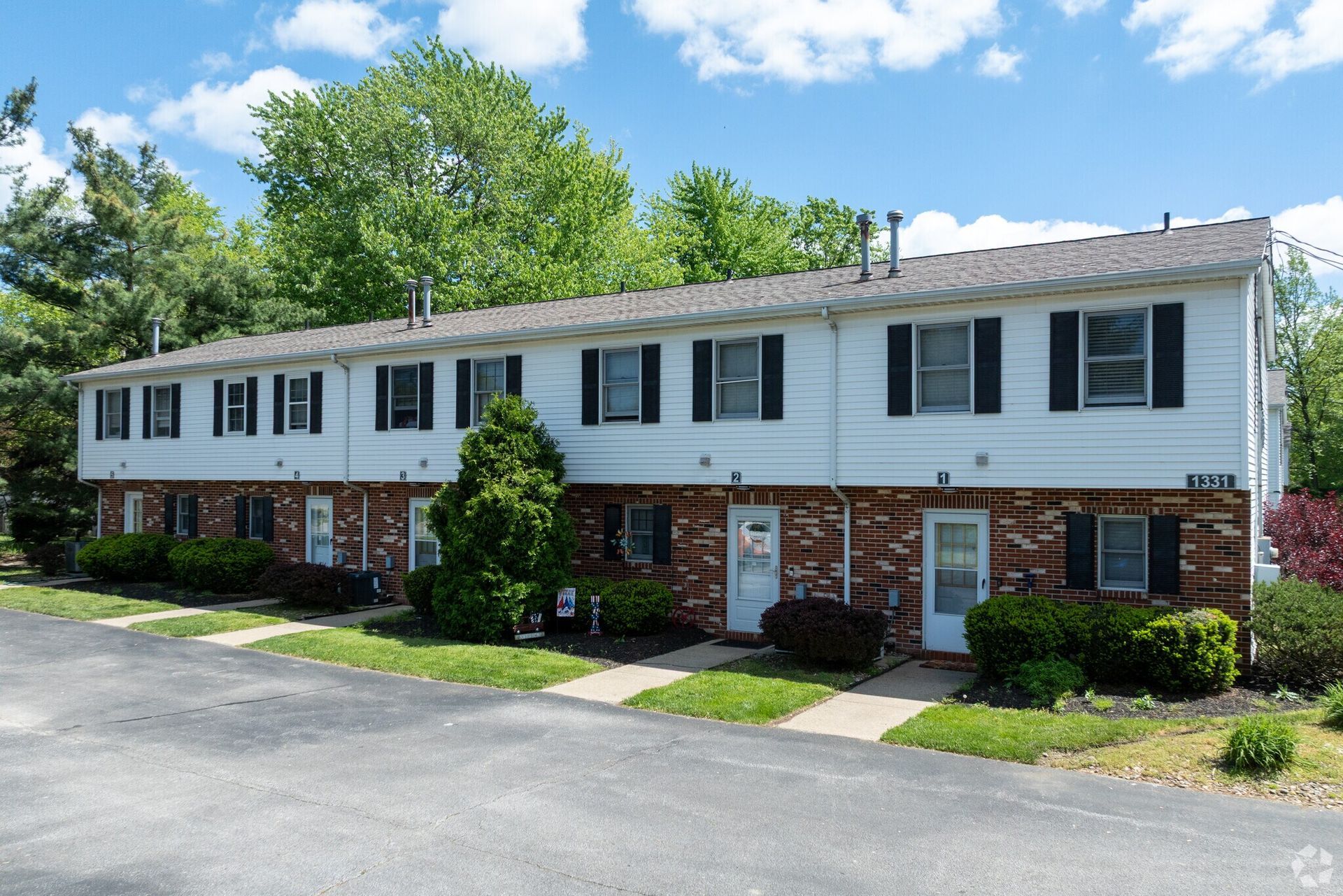Two-story townhouses with white siding and brick accents, surrounded by greenery.