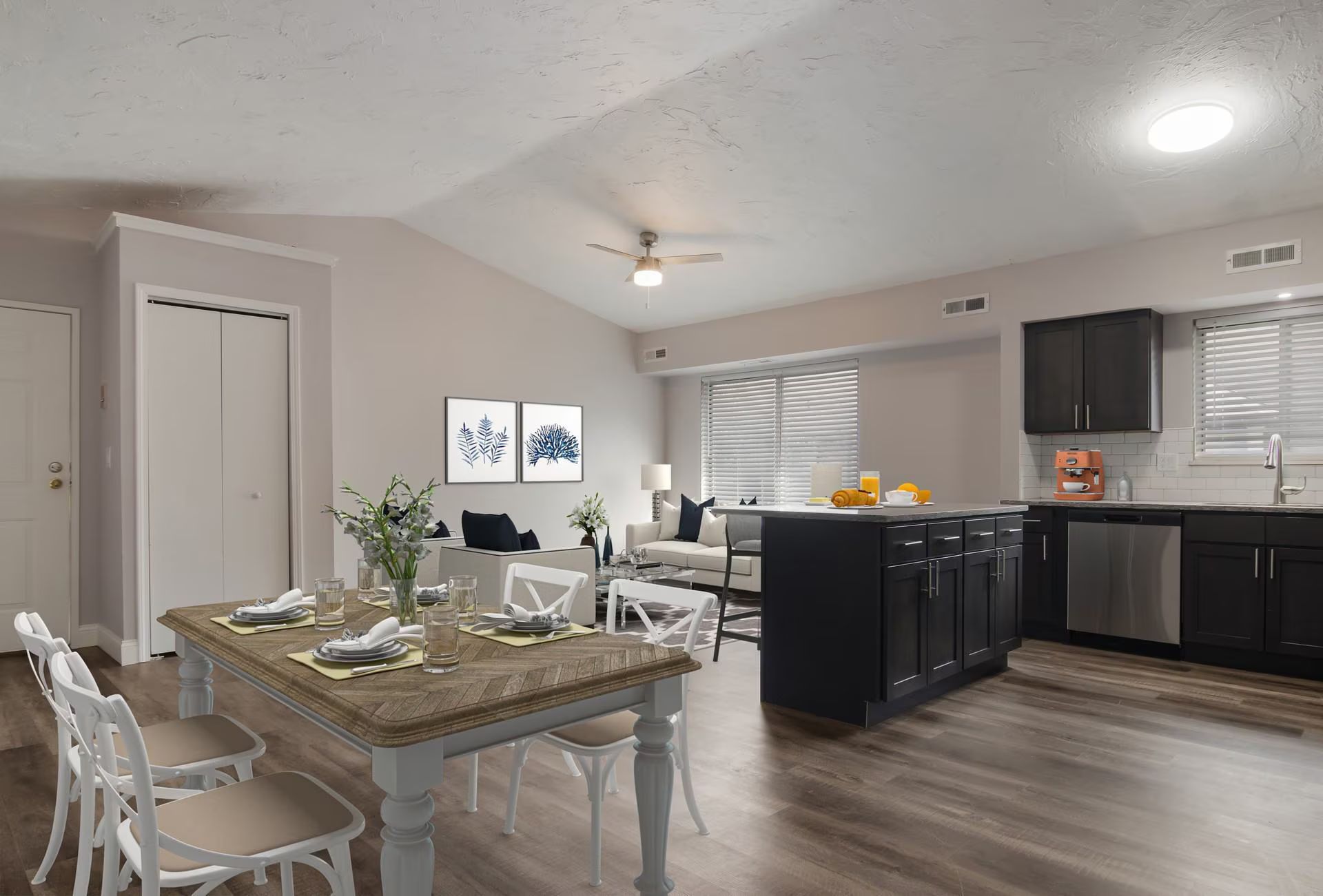 Open-concept kitchen, dining, and living area with wood floors, dark cabinets, and vaulted ceiling.