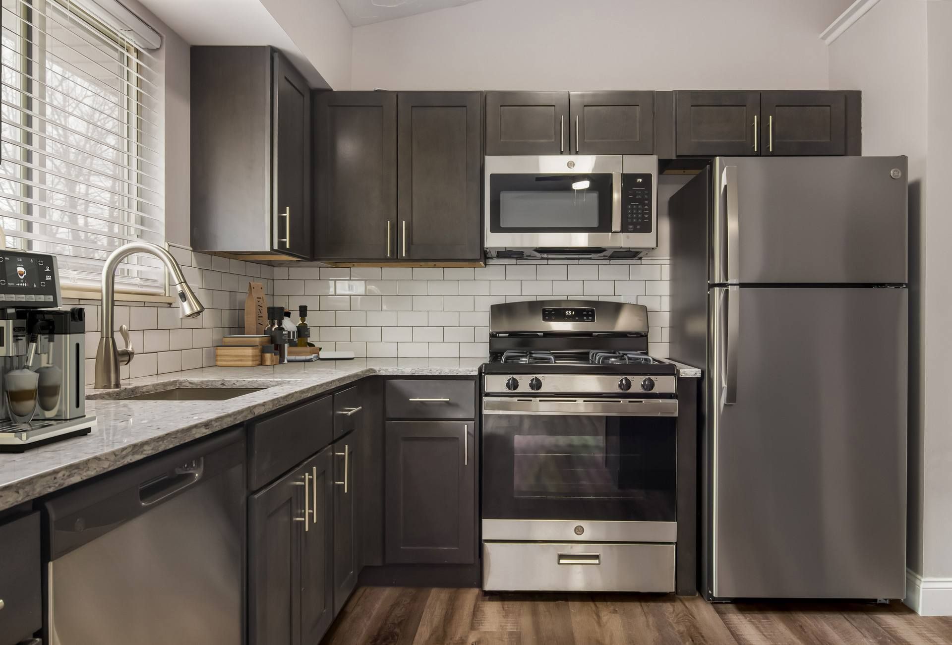 Modern kitchen with dark gray cabinets, stainless steel appliances, and wood-look flooring.