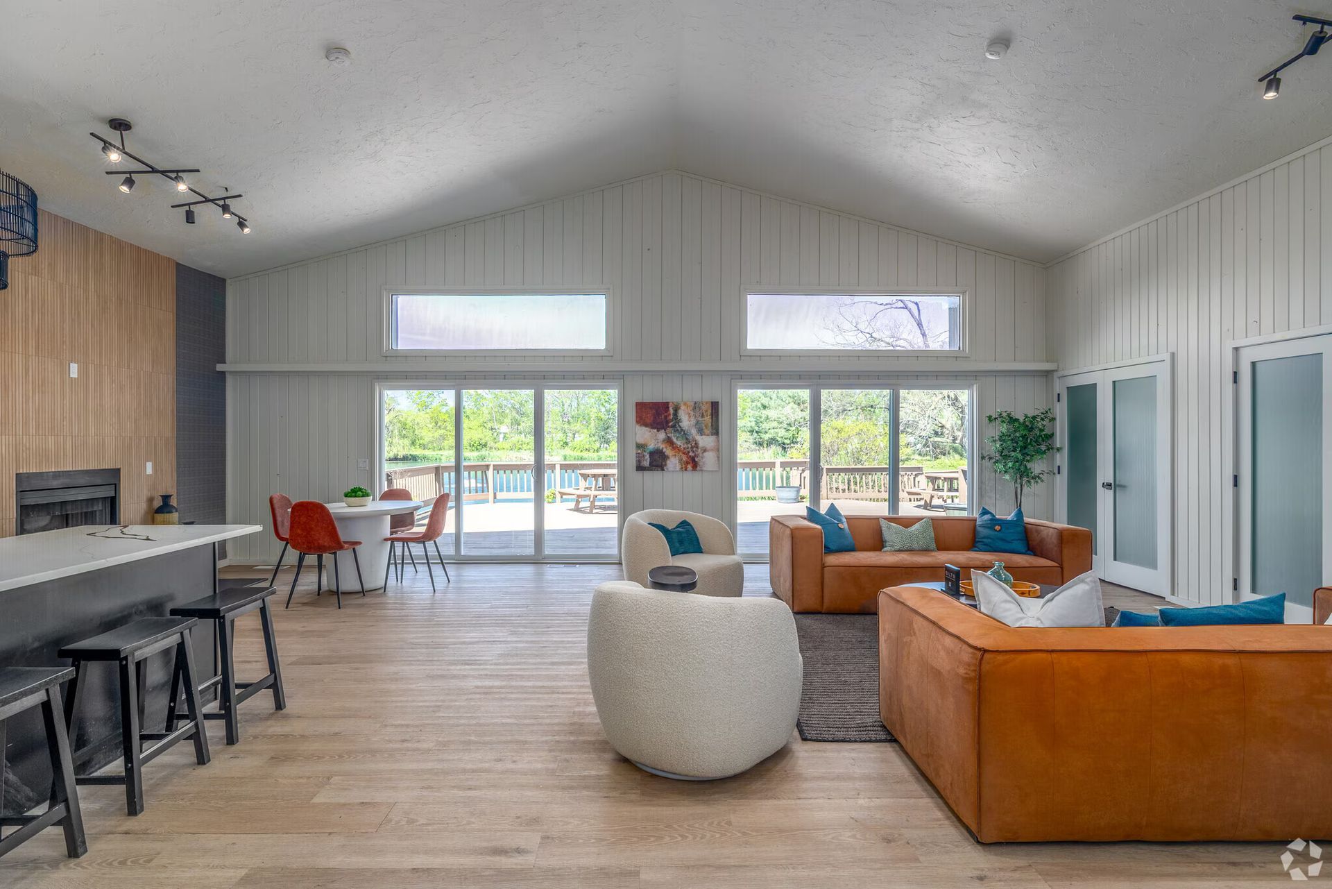 Spacious living room with high ceilings, white walls, and orange sofa, leading to a deck through glass doors.