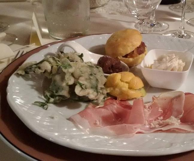 Piatto con antipasti assortiti: prosciutto, verdure fritte, pasta sfoglia ripiena e salsa.