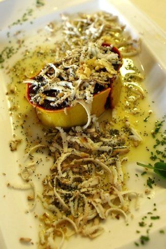 Antipasto con base gialla, guarnito con filamenti bianchi, puntini neri e salsa trasparente su un piatto bianco.