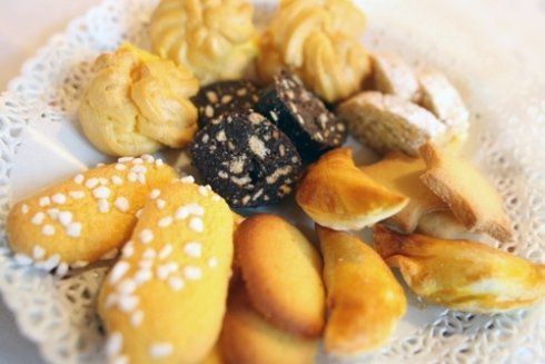 Pasticcini assortiti su un centrino bianco di pizzo. Include bignè, biscotti e altri prodotti da forno.