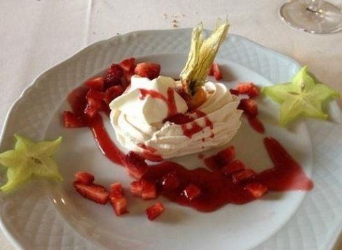 Dessert con panna montata, fragole, salsa e carambola su un piatto bianco.