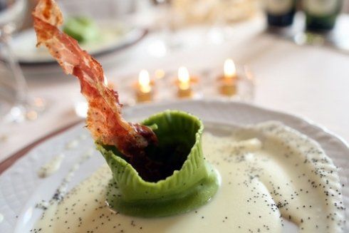 Primo piano di un piatto bianco con una struttura alimentare verde, besciamella e un pezzo di pancetta.