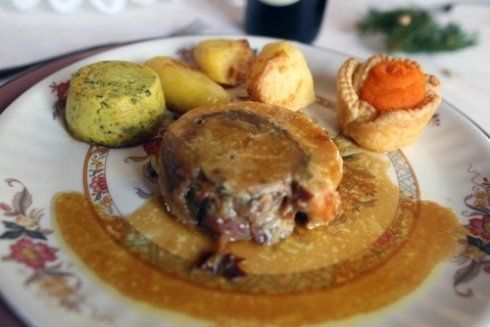Piatto di cibo: carne arrosto, patate, piatto di carote e contorno verde.
