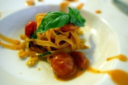 Piatto di pasta con pomodori e basilico su un piatto bianco, con salsa versata tutt'intorno.