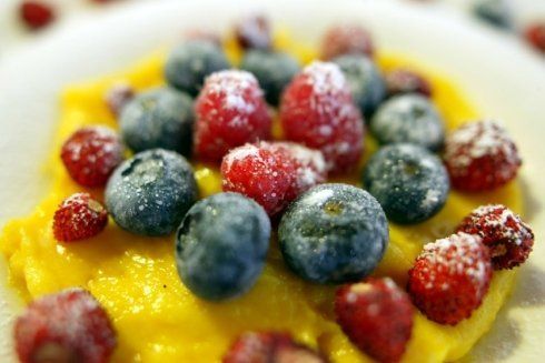 Bacche (mirtilli, lamponi e fragole) spolverate con zucchero a velo, su un letto di crema gialla.