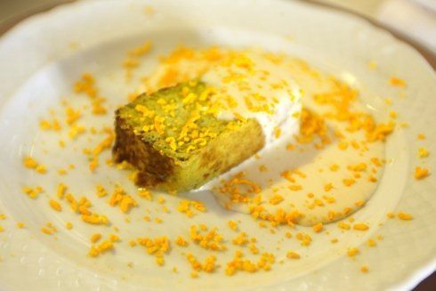 Fetta di torta verde e marrone con crema bianca e granelli arancioni su un piatto bianco.