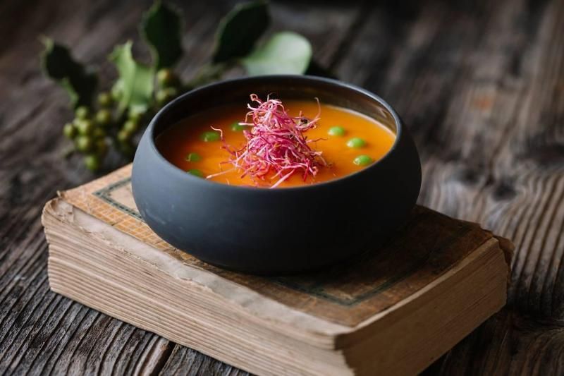 Ciotola nera di zuppa d'arancia con germogli e piselli su un vecchio libro. Tavolo di legno.