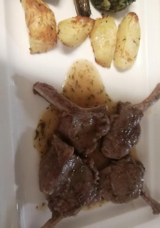 Costolette di agnello con salsa, patate arrosto e verdure su un piatto bianco.