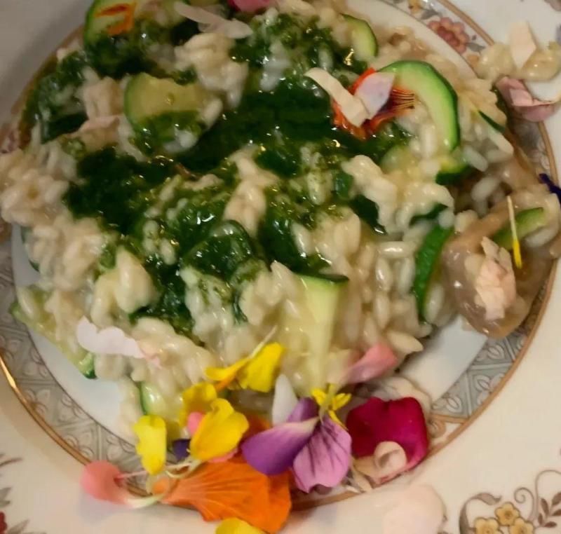 Risotto con zucchine e salsa verde, guarnito con fiori commestibili colorati su un piatto decorativo.