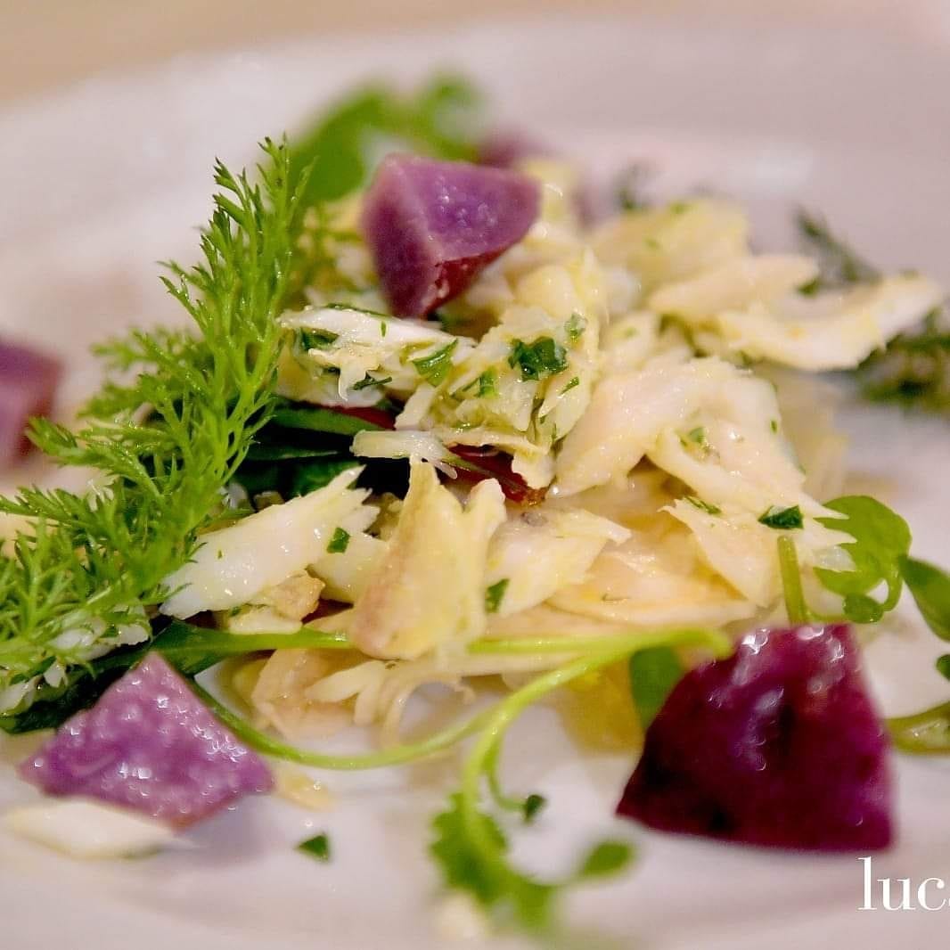 Insalata di pesce sfaldato, patate viola e verdure su un piatto bianco.