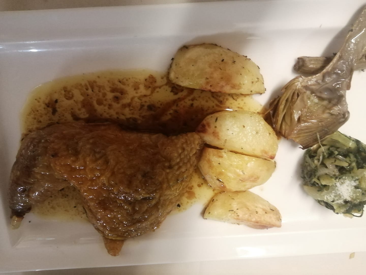 Anatra con patate e contorno di verdure in salsa, servita su un piatto bianco.