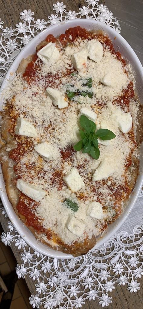 Melanzane alla parmigiana in una pirofila bianca ovale con mozzarella, formaggio grattugiato e basilico.