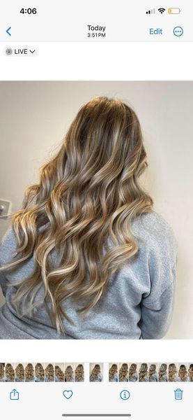 A woman with long wavy blonde hair is wearing a grey sweater.