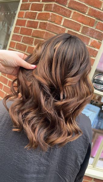 A woman is getting her hair done in front of a brick building.