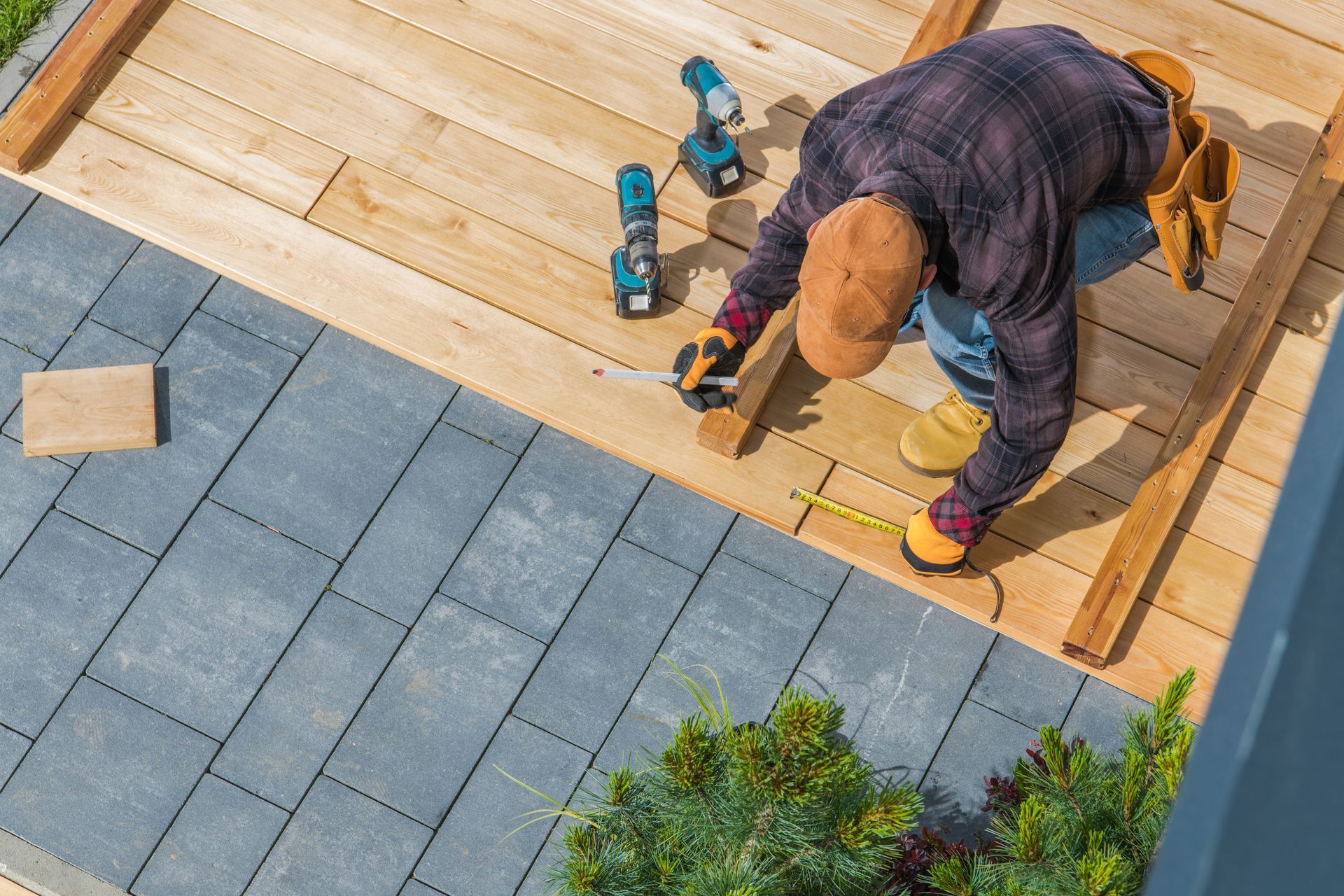 Worker laying wooden decking beside gray patio tiles with power tools nearby