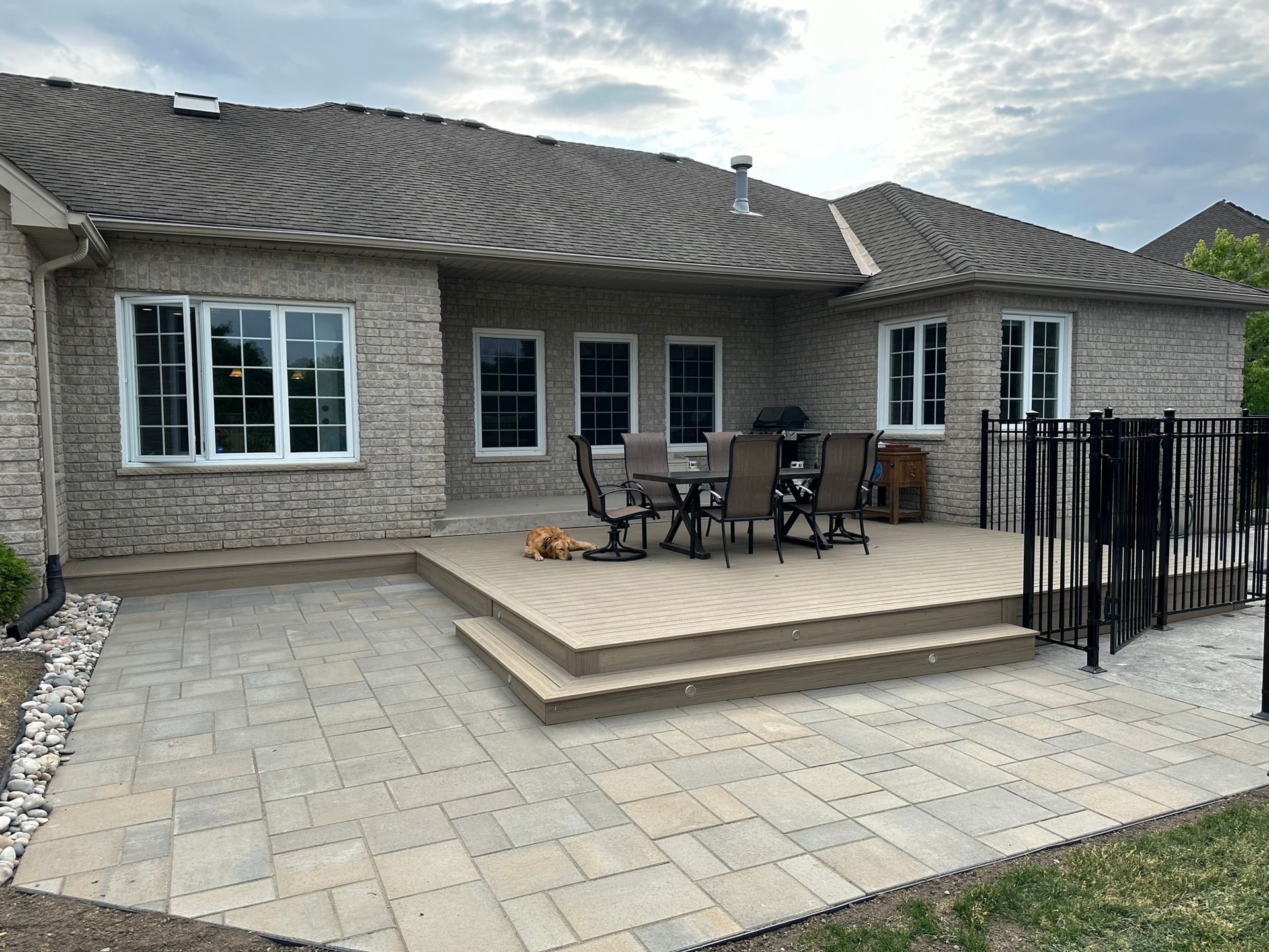 Backyard patio with a composite deck and dining set, next to a brick house.