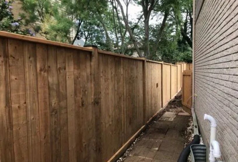 Wooden fence alongside a brick building, enclosing a narrow pathway.