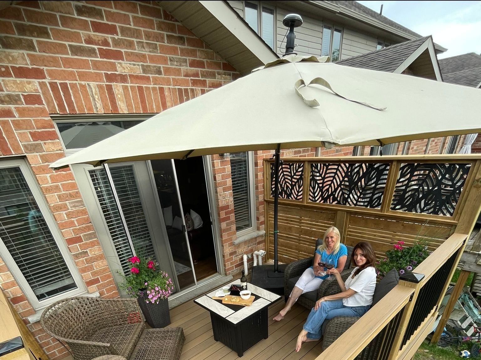 Two women are sitting on a deck under an umbrella.