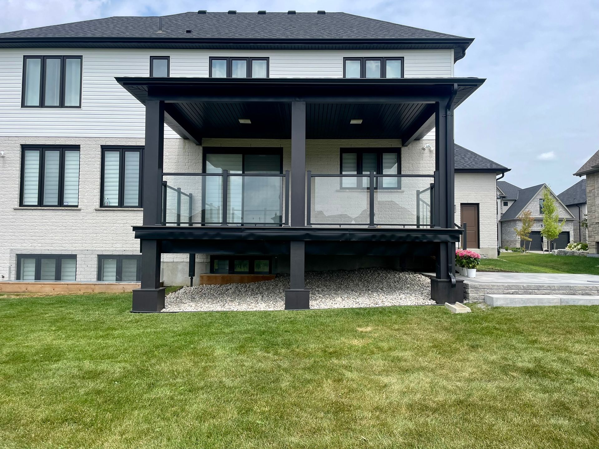 The back of a house with a large porch and a large lawn in front of it.