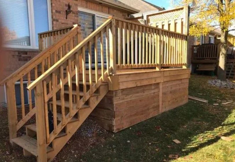 Wooden deck with stairs, railing, and a lattice fence backdrop in a backyard setting.