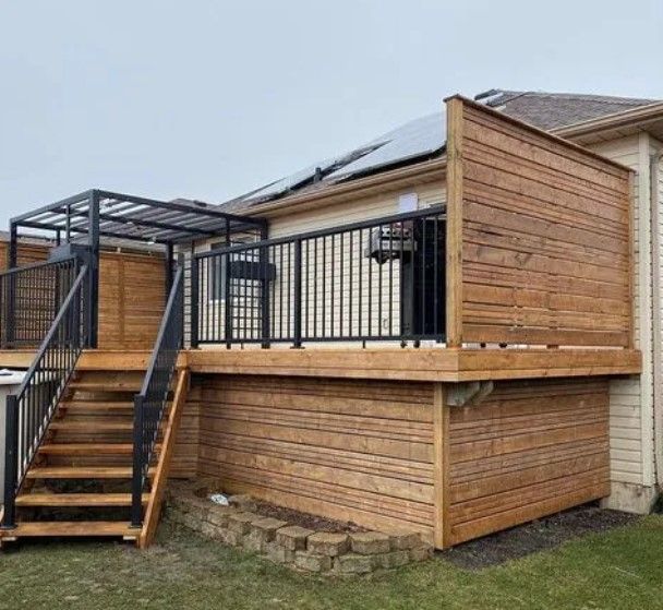 Wooden deck with black railings and stairs. A privacy screen and pergola are visible.